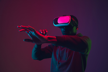 Image showing African-american man\'s portrait in VR-headset isolated on gradient studio background in neon light