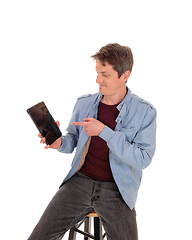Image showing Young man sitting on chair pointing to his tablet