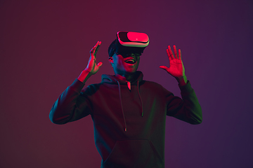 Image showing African-american man\'s portrait in VR-headset isolated on gradient studio background in neon light