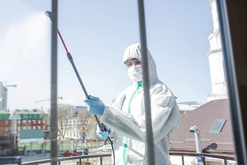 Image showing Coronavirus Pandemic. A disinfector in a protective suit and mask sprays disinfectants in the house or office