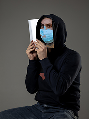 Image showing Be safe and read to become someone else - man covering face with book in face mask while reading on grey background