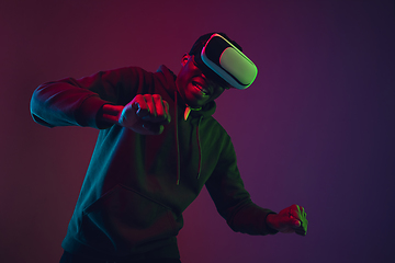 Image showing African-american man\'s portrait in VR-headset isolated on gradient studio background in neon light