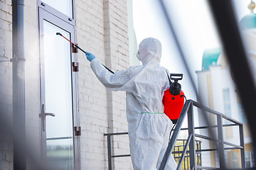 Image showing Coronavirus Pandemic. A disinfector in a protective suit and mask sprays disinfectants in the house or office