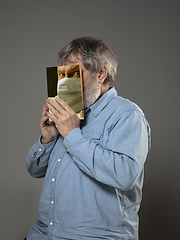 Image showing Be safe and read to become someone else - man covering face with book in face mask while reading on grey background