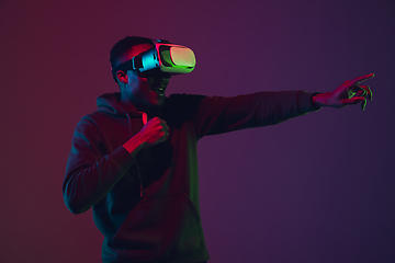 Image showing African-american man\'s portrait in VR-headset isolated on gradient studio background in neon light