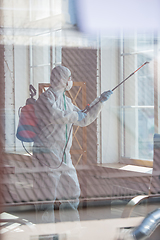 Image showing Coronavirus Pandemic. A disinfector in a protective suit and mask sprays disinfectants in the house or office