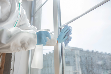 Image showing Coronavirus Pandemic. A disinfector in a protective suit and mask sprays disinfectants in the house or office