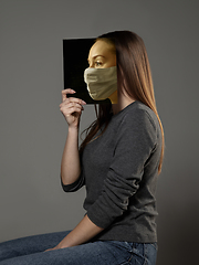 Image showing Be safe and read to become someone else - woman covering face with book in face mask while reading on grey background