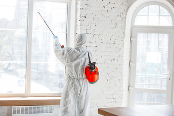 Image showing Coronavirus Pandemic. A disinfector in a protective suit and mask sprays disinfectants in the house or office