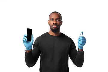 Image showing How coronavirus changed our lives. Young man disinfecting gadgets surfaces on white background