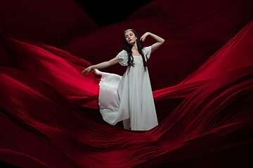 Image showing Young and graceful ballet dancer on billowing red cloth background in classic action. Art, motion, action, flexibility, inspiration concept.