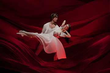 Image showing Young and graceful ballet dancers on billowing red cloth background in classic action. Art, motion, action, flexibility, inspiration concept.