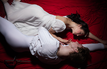 Image showing Young and graceful ballet dancers on billowing red cloth background in classic action. Art, motion, action, flexibility, inspiration concept.