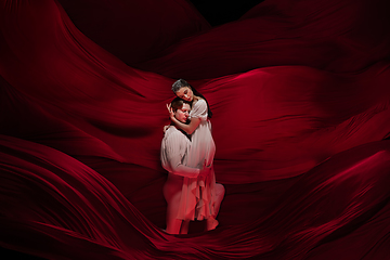 Image showing Young and graceful ballet dancers on billowing red cloth background in classic action. Art, motion, action, flexibility, inspiration concept.