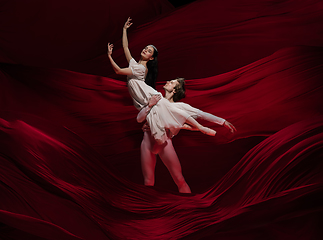 Image showing Young and graceful ballet dancers on billowing red cloth background in classic action. Art, motion, action, flexibility, inspiration concept.