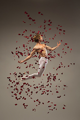 Image showing Young and graceful ballet dancer on studio background with rose petals. Art, motion, action, flexibility, inspiration concept.