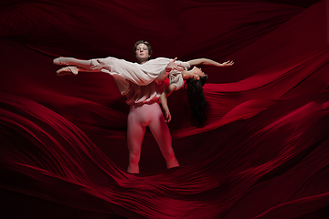 Image showing Young and graceful ballet dancers on billowing red cloth background in classic action. Art, motion, action, flexibility, inspiration concept.