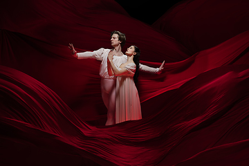 Image showing Young and graceful ballet dancers on billowing red cloth background in classic action. Art, motion, action, flexibility, inspiration concept.