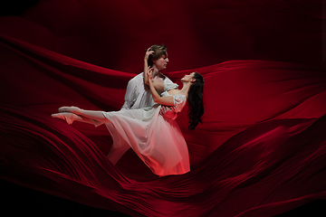 Image showing Young and graceful ballet dancers on billowing red cloth background in classic action. Art, motion, action, flexibility, inspiration concept.