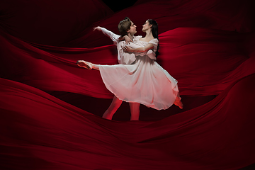 Image showing Young and graceful ballet dancers on billowing red cloth background in classic action. Art, motion, action, flexibility, inspiration concept.