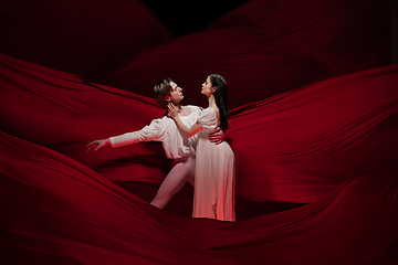 Image showing Young and graceful ballet dancers on billowing red cloth background in classic action. Art, motion, action, flexibility, inspiration concept.