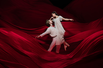 Image showing Young and graceful ballet dancers on billowing red cloth background in classic action. Art, motion, action, flexibility, inspiration concept.