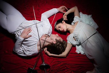 Image showing Young and graceful ballet dancers on billowing red cloth background in classic action. Art, motion, action, flexibility, inspiration concept.