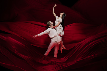 Image showing Young and graceful ballet dancers on billowing red cloth background in classic action. Art, motion, action, flexibility, inspiration concept.