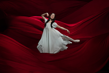 Image showing Young and graceful ballet dancer on billowing red cloth background in classic action. Art, motion, action, flexibility, inspiration concept.