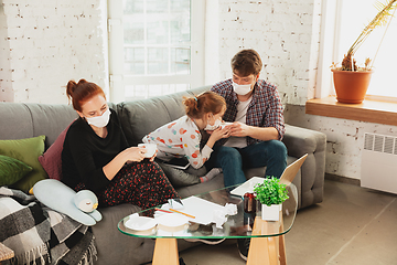 Image showing Caucasian family in protective masks and gloves isolated at home with coronavirus symptoms, stop epidemic