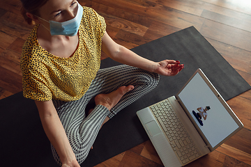 Image showing Sporty young woman taking yoga lessons online and practice at home while being quarantine