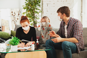 Image showing Caucasian family in protective masks and gloves isolated at home with coronavirus symptoms, treatment