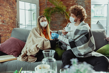 Image showing Woman and man, couple in protective masks and gloves isolated at home with coronavirus symptoms