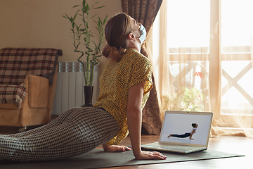 Image showing Sporty young woman taking yoga lessons online and practice at home while being quarantine