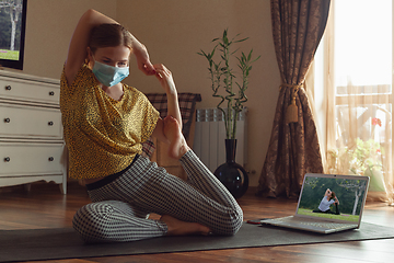 Image showing Sporty young woman taking yoga lessons online and practice at home while being quarantine