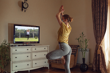 Image showing Sporty young woman taking yoga lessons online and practice at home while being quarantine