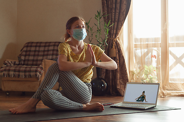 Image showing Sporty young woman taking yoga lessons online and practice at home while being quarantine