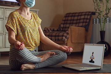 Image showing Sporty young woman taking yoga lessons online and practice at home while being quarantine