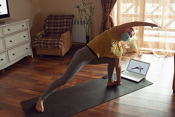 Image showing Sporty young woman taking yoga lessons online and practice at home while being quarantine