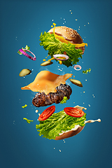 Image showing Hamburger with flying ingredients on blue studio background. Fast food, cuisine concept.