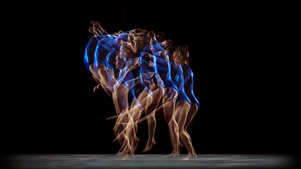 Image showing Young flexible girl on black studio background in strobe and neon light. Young female model practicing artistic gymnastics.