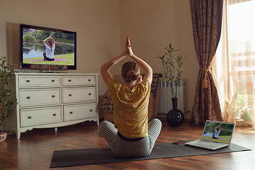 Image showing Sporty young woman taking yoga lessons online and practice at home while being quarantine