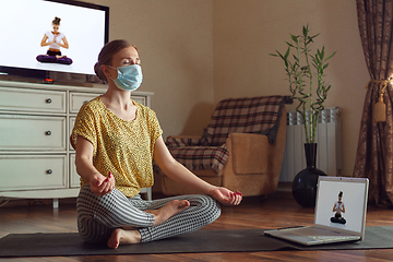 Image showing Sporty young woman taking yoga lessons online and practice at home while being quarantine