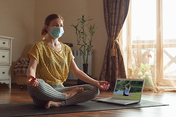 Image showing Sporty young woman taking yoga lessons online and practice at home while being quarantine