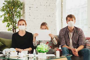 Image showing Caucasian family in protective masks and gloves isolated at home with coronavirus symptoms, stop epidemic