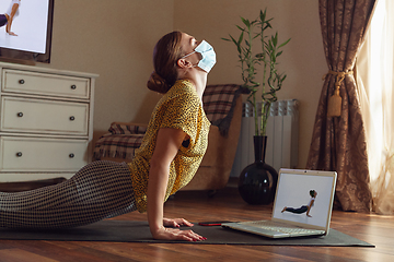 Image showing Sporty young woman taking yoga lessons online and practice at home while being quarantine