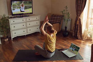 Image showing Sporty young woman taking yoga lessons online and practice at home while being quarantine