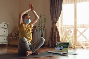 Image showing Sporty young woman taking yoga lessons online and practice at home while being quarantine