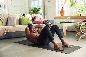 Image showing Young african-american man teaching at home online courses of fitness, aerobic, sporty lifestyle while being quarantine