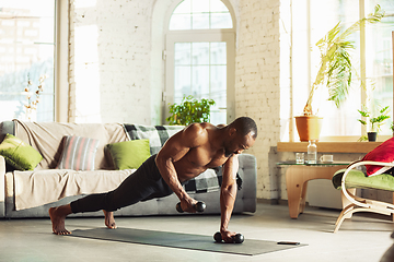 Image showing Young african-american man teaching at home online courses of fitness, aerobic, sporty lifestyle while being quarantine